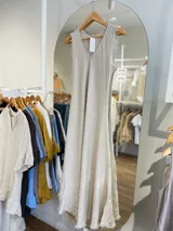 Vestido largo de lino en color beige, sin mangas y con escote en V. Presenta un diseño de corte holgado con terminaciones deshilachadas en las sisas y el ruedo.