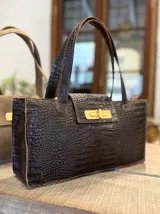 Bolso tote marrón con textura símil cocodrilo, cierre dorado y doble asa de mano.