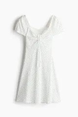 Vestido corto blanco con estampado floral celeste, de punto acanalado con escote corazón ribeteado en encaje y cordón para ajustar en el centro del busto. Modelo de manga corta con cuerpo entallado, copas preformadas y pollera con vuelo.