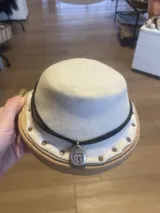 Sombrero de ala corta color crema, con cinta negra y dije plateado.