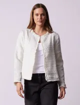 Chaqueta cruda de tejido boucle con flecos en el borde y botones negros en los puños.
