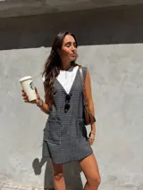 Vestido corto tipo jumper, confeccionado en tejido escocés a cuadros en tonos grises y blancos. Sin mangas, con escote en V y bolsillos delanteros. Se puede usar solo o con remera debajo.