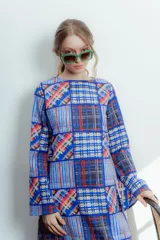 Vestido largo de crepe estampado con diseño patchwork en tonos azules, rojos y blancos. Tiene cuello redondo, mangas largas acampanadas y corte recto.