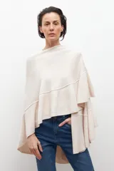 Capa tejida color crudo, de manga larga y corte amplio, con detalle de volados en los bordes.