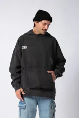 Buzo canguro negro de frisa rústica con corte oversize y capucha. Presenta un pequeño logo blanco en el pecho y un bolsillo tipo canguro.