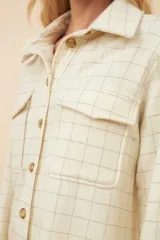 Camisa estilo leñador color beige con textura de espiga, de manga larga con puños abotonados, cuello clásico, cierre frontal con botones y dos bolsillos de parche con solapa abotonada en el pecho.