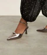 Zapato de tacón color gris con punta fina, tira fina con hebilla en el tobillo y detalle de nudo con strass.