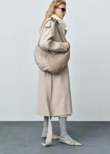 Trench color beige con solapas, trabillas en los hombros y puños, cinturón desmontable y bolsillos laterales.