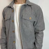 Sobrecamisa gris con diseño de espiga, cuello clásico, cierre frontal abotonado, dos bolsillos con solapa en el pecho y corte recto.