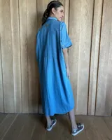 Vestido túnica celeste de lino con rayas verticales blancas, corte recto, cuello camisero y mangas cortas.