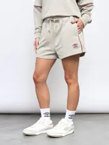 Short deportivo color beige, marca Umbro, de felpa sin frisa con cintura elastizada y cordón ajustable. Presenta ribete color borgoña en los laterales y logo de la marca bordado en el muslo izquierdo.