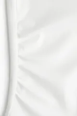 Top blanco de punto, ajustado al cuerpo, con escote Bardot (hombros descubiertos) y frunces laterales que crean un efecto drapeado.