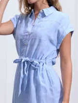 Vestido camisero corto con estampado de rayas verticales celestes y blancas. Tiene cuello camisero, mangas cortas con dobladillo, cierre frontal con botones y cinturón de lazo en la cintura.