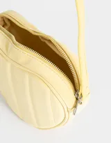 Bandolera negra en forma de corazón, confeccionada en cuerina acolchada con pespuntes verticales. Tiene correa larga regulable y cierre superior.