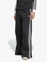Pantalón de sudadera Adidas de corte ancho, color negro con tres rayas blancas verticales en los laterales y logo bordado en la parte superior. Confeccionado en tejido de felpa francesa.