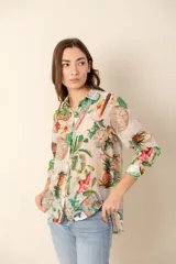 Camisa estampada con cuello clásico, cierre frontal con botones y mangas largas. El estampado presenta motivos tropicales como flores, hojas y piñas.