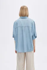 Camisa celeste de manga corta, corte holgado, con cuello camisero y cierre frontal con botones.