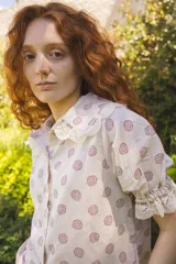 Camisa color crema con estampado de flores rojas, cuello babero y mangas cortas abullonadas con detalles de encaje.