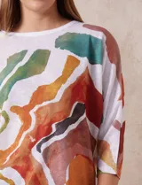 Buzo blanco con estampado abstracto en tonos naranja, verde, marrón y rojo. Tiene cuello redondo y mangas 3/4.