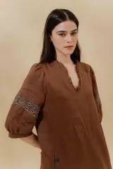 Vestido largo color beige, confeccionado en lino, con escote en V con volados y apliques de puntilla en las mangas. Posee bolsillos delanteros y tajos laterales.