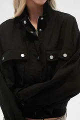 Campera color beige de manga larga, con cuello alto, cierre frontal con cremallera y botones a presión, bolsillos con solapa en el pecho y puños con trabilla ajustable.