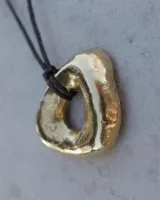 Collar con dije dorado irregular con agujero central, colgando de cordón negro ajustable.