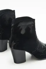 Botín negro de gamuza con apliques de cuero texturizado y remaches. Tiene cierre en el talón y taco cuadrado.