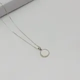 Conjunto de cadena y dije plateados. El dije es una medalla redonda con borde de pequeñas circonias y centro liso.