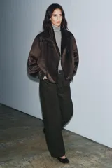 Cazadora de estilo aviador con cuello subido, manga larga y cierre frontal asimétrico con cremallera. Presenta un diseño de doble faz con exterior de efecto ante y forro interior de borreguillo a tono, con detalles de ribetes en cuero sintético.