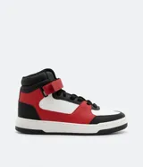Championes de caña alta, color blanco, rojo y negro, con ajuste de cordones y velcro. Suela bicolor y puntera redondeada.