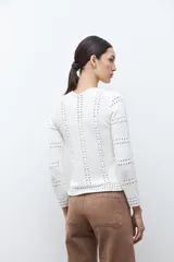 Chaqueta de tejido punto color blanco crudo, de manga larga y cuello redondo, con cierre frontal metálico. Presenta un diseño calado con aberturas verticales a lo largo del cuerpo y las mangas.