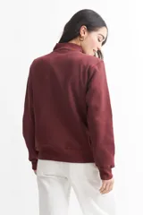 Campera color bordó de felpa liviana, con cuello alto, cierre frontal, bolsillos laterales y puños y cintura acanalados.