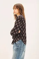 Camisa negra con estampado floral blanco, de corte regular, con volados en el cuello y cierre frontal con botones.