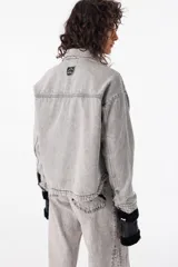 Camisa corta de jean azul con terminación redondeada en el ruedo. Presenta dos bolsillos plaqué bordados con motivo de montaña y detalle de pespunte a contratono.