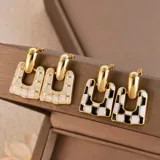 Par de aros colgantes con diseño geométrico. Un aro es color crema con detalles dorados, el otro es blanco y negro con detalles dorados.