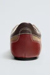 Zapato deportivo de piel color marrón claro con detalles en marrón oscuro y rojo. Presenta pespuntes en contraste, suela plana y cierre con cordones de colores. Colaboración especial Harry Lambert for Zara x Disney.
