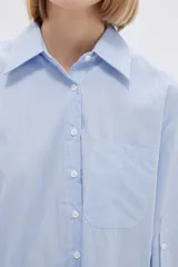 Camisa a rayas verticales verdes y blancas, de corte holgado, manga larga con puños abotonados, cuello clásico y bolsillo de parche en el pecho.
