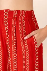 Pantalón de corte recto color rojo con estampado de cadenas doradas, pretina elástica, cierre y broche al frente, pinzas y bolsillos laterales.