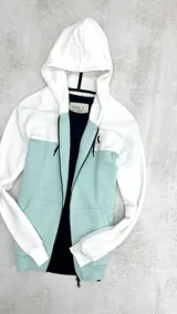 Campera con capucha blanca y turquesa con cierre frontal y bolsillos tipo canguro.