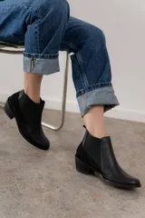 Botín negro de cuero con paneles laterales de gamuza y elástico en los tobillos. Tiene un pequeño taco cuadrado.