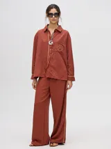 Conjunto camisero color ladrillo, compuesto por una camisa de corte holgado con logo bordado en el bolsillo y un pantalón de pierna ancha con raya lateral.