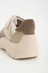 Zapatilla urbana de mujer con plataforma gruesa, combinando paneles de cuero en tonos beige, blanco roto y marrón topo. Presenta cordones anchos y un detalle de texto en el talón.