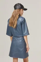 Mini de cuero azul con cintura alta y corte en A, con cierre metálico lateral y bolsillos traseros.
