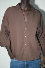 Camisa marrón de popelina con cuello solapa, escote en pico, cierre frontal con botones y mangas anchas con puños.