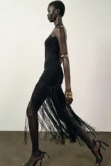 Vestido largo negro de tejido elástico, con escote halter y bajo con flecos a tono.