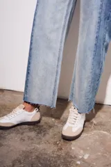 Jean de tiro medio, corte recto y largo cropped, confeccionado en denim de algodón con elastano. Presenta un efecto de lavado bicolor o combinado, con paneles de diferente tono de azul claro, y costuras verticales marcadas en el frente. El ruedo es deshilachado.