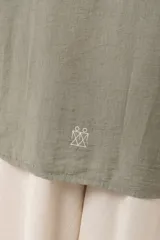 Camisa verde militar de manga larga con silueta oversize, dos bolsillos delanteros y corte levemente más largo en la espalda. Escote en V abotonado con detalle de galón picot a lo largo de la cartera y botones a tono. Isotipo bordado en la parte trasera.