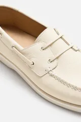 Zapato náutico color crema de cuero, con cordones alrededor del tobillo y suela plana.