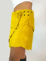 Minifalda amarilla de cuero con diseño irregular y cierre lateral con hebilla.
