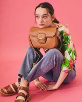 Bandolera color beige con textura símil reptil, cierre con broche metálico dorado y correa larga regulable.